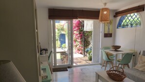 Una stanza con zona pranzo, divano, tavolo con cesto e vista su un giardino con fiori rosa.