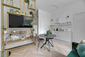 A modern living room with a TV, dining table, and chairs, a green sofa, and a kitchen with white cabinets and appliances. - Tokio Premium w centrum Sopotu (Sopot)