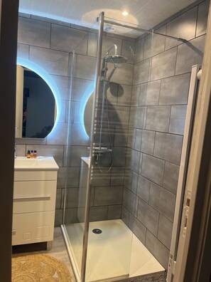 Ein modernes Badezimmer mit einer einachigen Duschkabine, einem Waschtisch inklusive Spiegel und einer runden Deckenleuchte.