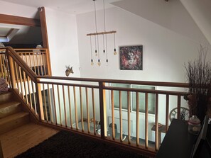 Eine Treppe mit Holelllaufgeländern, die zu einer oberen Etage führt, ein Essbereich mit Tisch und Stühlen, eine wandmontierte Leuchte und ein gerahmtes abstraktes Gemälde.