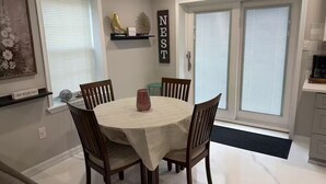 Een eetruimte met een ronde tafel, vier stoelen, een vaas en een wandplank met decoratieve objecten.