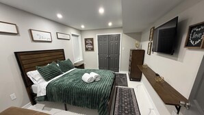 Een slaapkamer met een bed, nachtkastje, bankje, kledingkast, televisie en motiverende wanddecoratie.