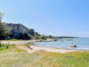 Ett kustlandskap med en klippig brant, en sandstrand och stilla vatten.