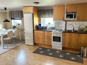 A compact kitchen with wooden cabinets, a white refrigerator, a microwave, a stove, and a sink.