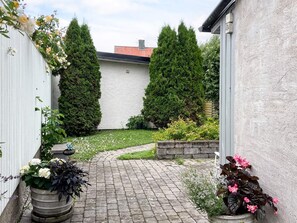 A paved pathway leading to a white building with a brick roof, surrounded by greenery and potted plants. - 4 Star Holiday Home in Visby (Visby)