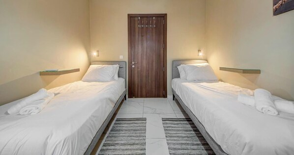 Una habitación de hotel con dos camas individuales, una puerta de madera y una alfombra pequeña.