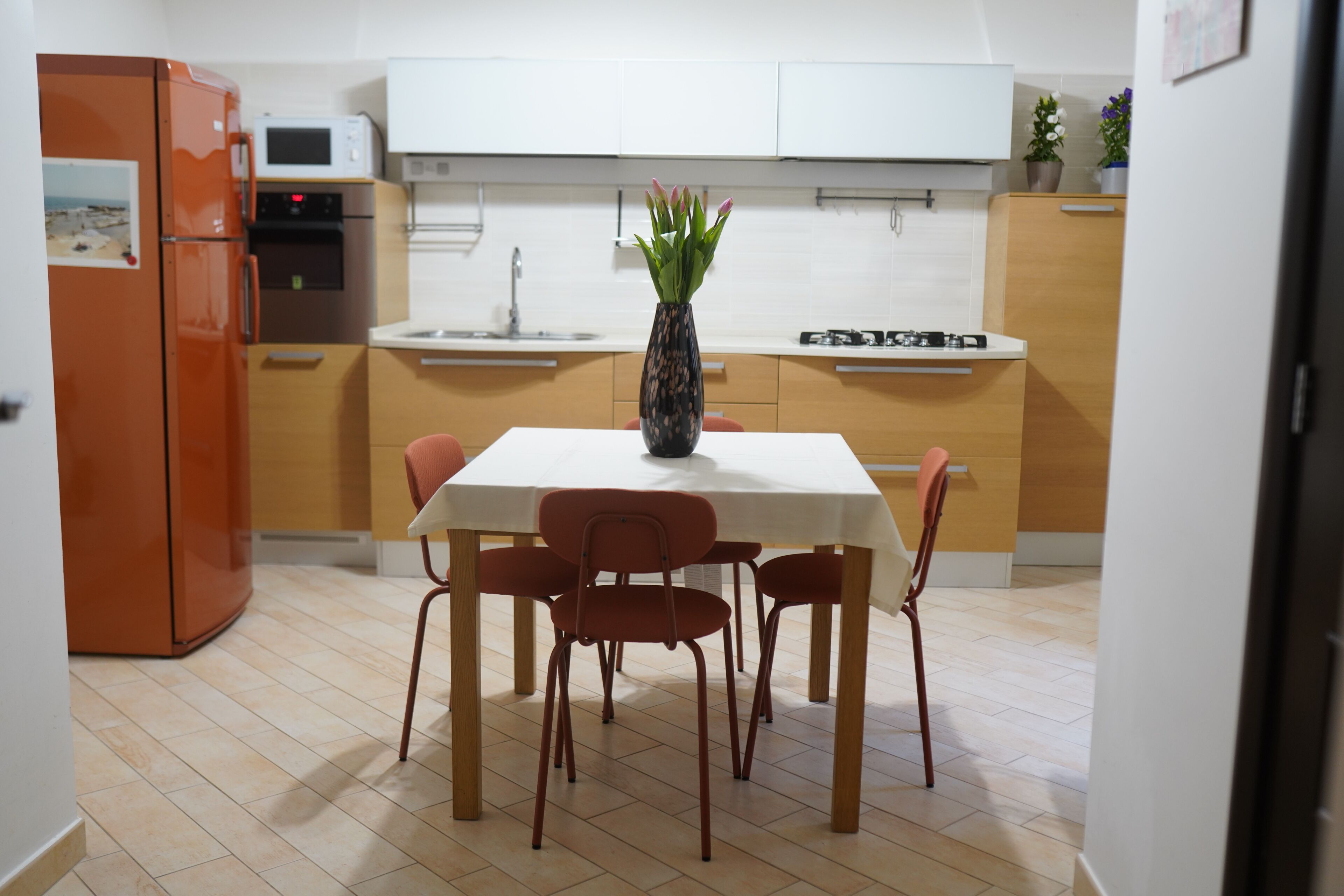 Una cocina moderna con una mesa de comedor, sillas, un jarrón con flores y un microondas.