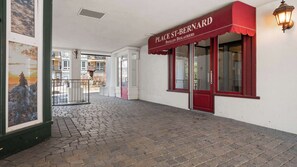 Ein Gebäudeeingang mit roter Markise, auf der 'PLACE ST-BERNARD' steht, und einem Kopfsteinpflasterweg, der zu einer Glastür führt.