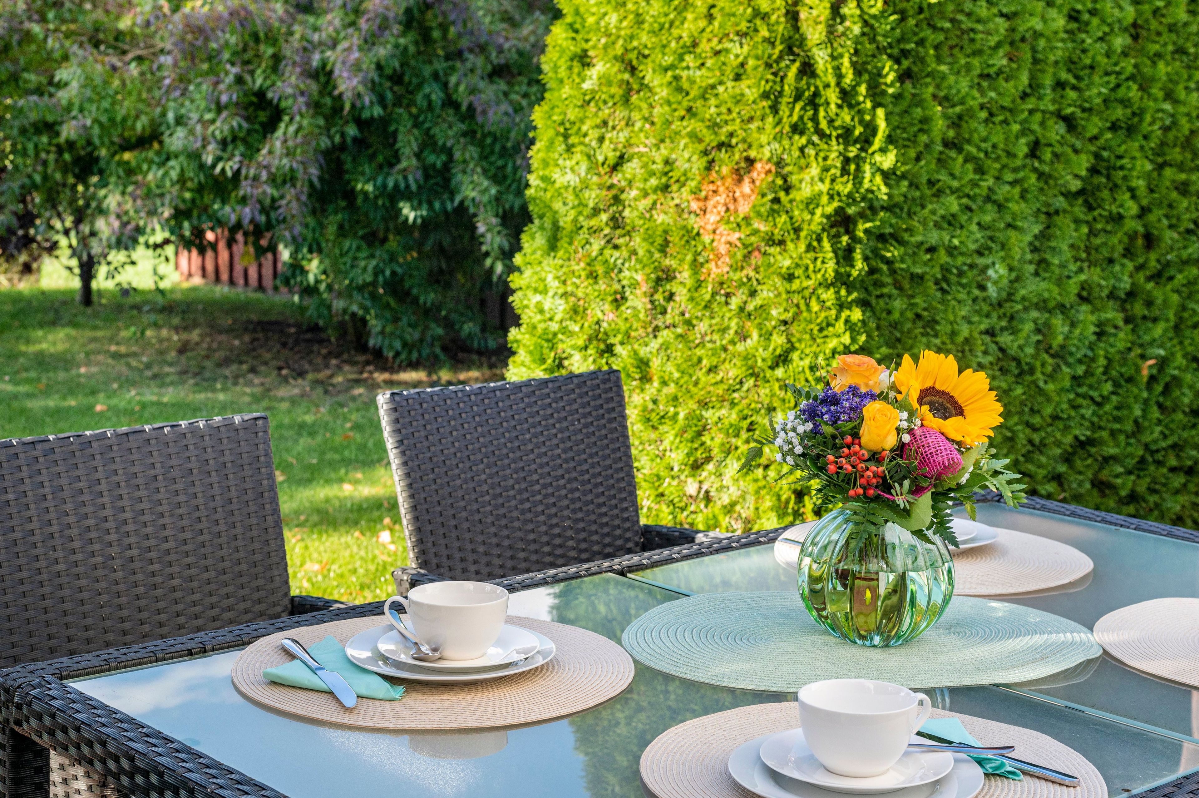 An outdoor dining area with wicker chairs, a glass table, and a vase of flowers.
