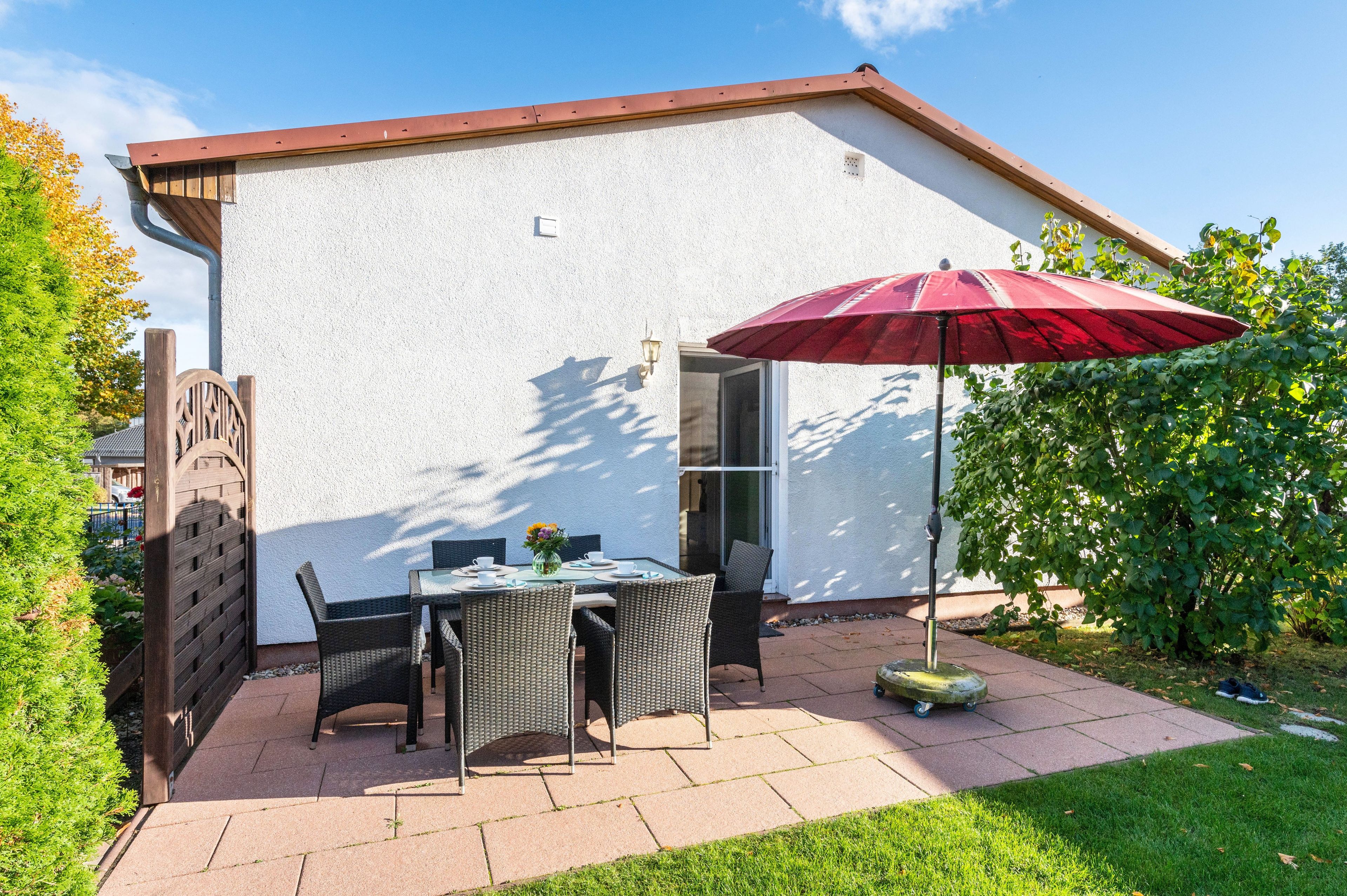 Eine Terrasse mit Tisch und Stühlen, einem roten Sonnenschirm und einem kleinen Garten.