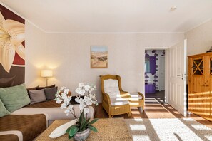 A living room with a sofa, a wicker chair, a table with a plant, and a painting on the wall. - Holiday Home Pepe for 4 Guests (70 m²) in Göhren-Lebbin (Göhren-Lebbin)