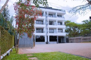 A multi-story building with balconies, a paved courtyard, and a grassy area with trees. - Mbugani View Suites (Nairobi)