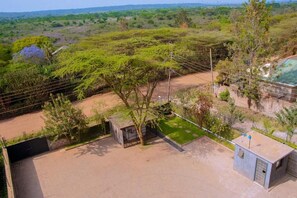 A fenced property with a paved area, a small building, and a view of a green landscape. - Mbugani View Suites (Nairobi)
