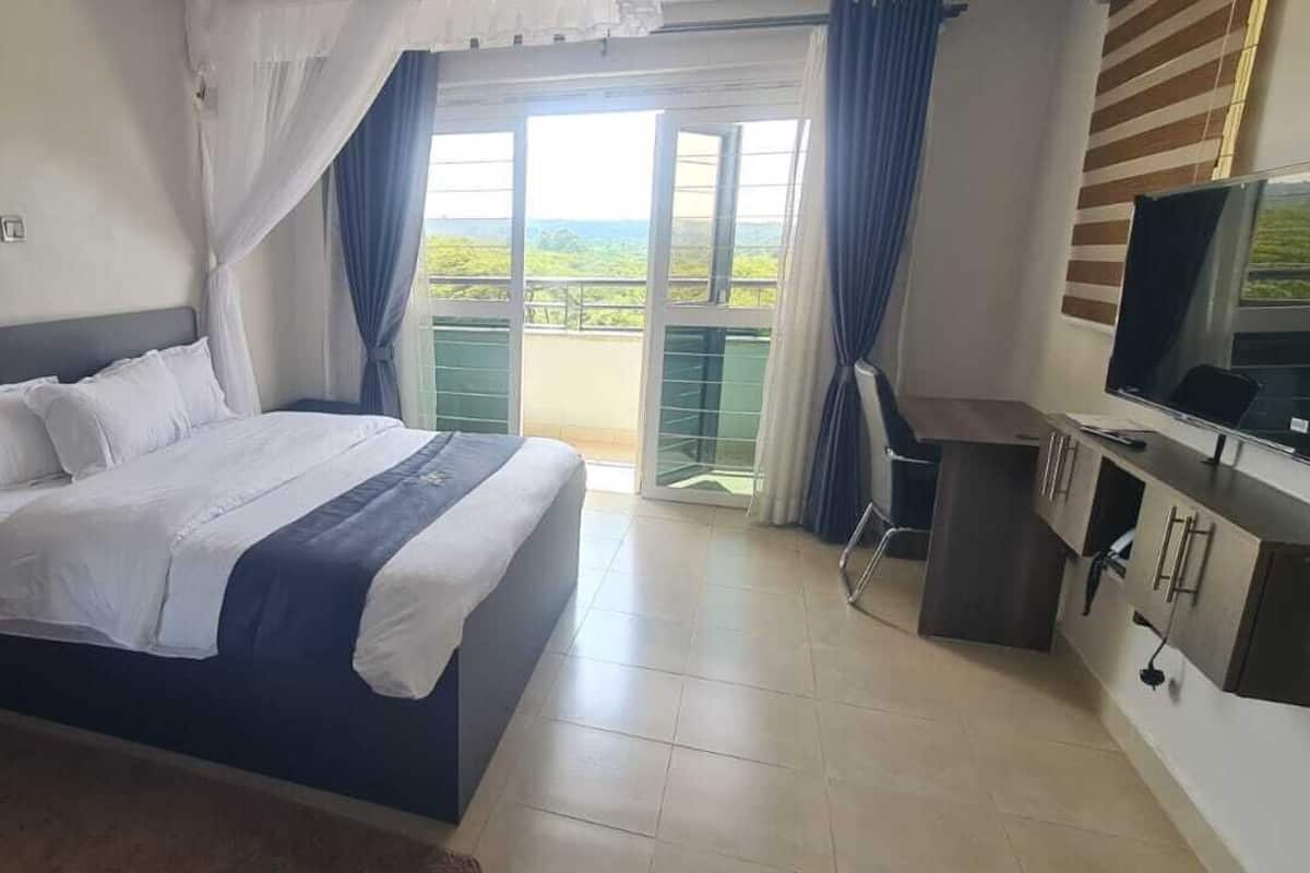 A bedroom with a bed, a TV, a desk, and a balcony with a view.