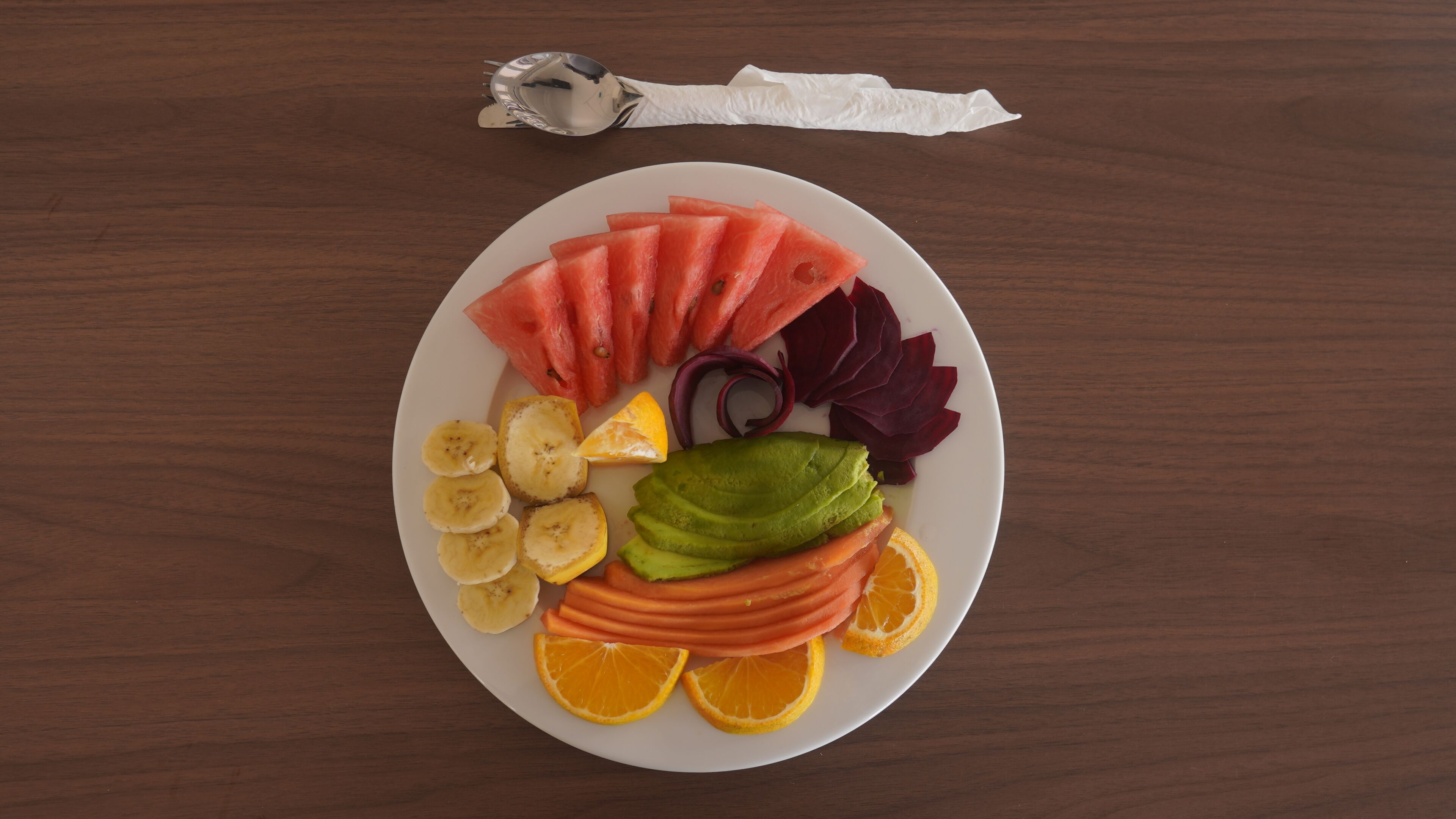 Un plato de frutas y verduras cortadas sobre una mesa de madera.