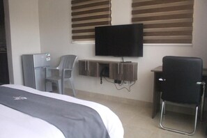 A hotel room with a bed, a desk, a chair, a television, and a minibar. - Mbugani View Suites (Nairobi)