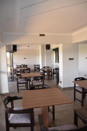 A dining area with multiple tables and chairs, a high ceiling, and a clean, white interior. - Mbugani View Suites (Nairobi)