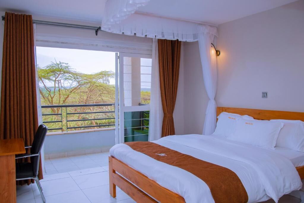 A bedroom with a bed, a desk, and a view of trees through a window.