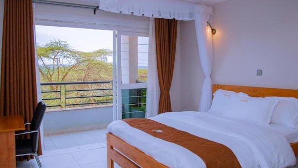 Une chambre à coucher avec un lit, un bureau et une vue sur les arbres par la fenêtre.