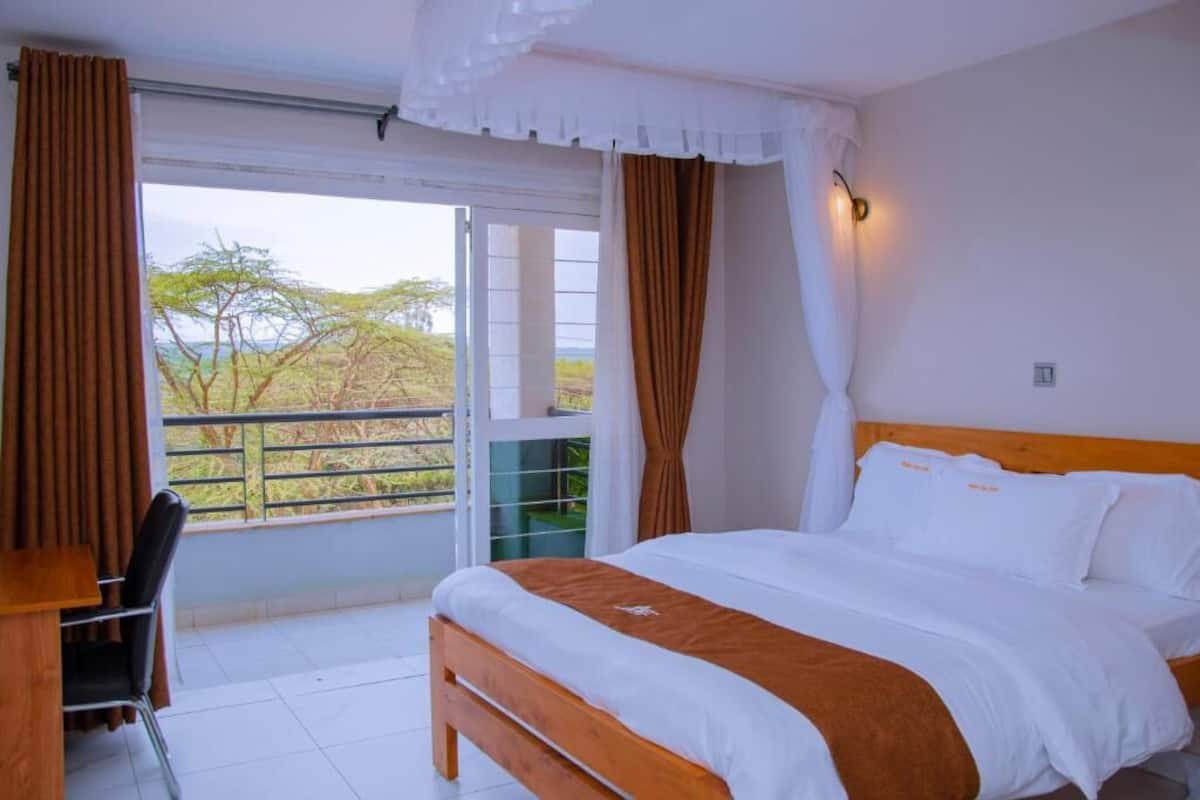 A bedroom with a bed, a desk, and a view of trees through a window.