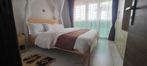 Ein Bett mit Baldachin, ein Holz-Kopfteil, ein Nachttisch, ein Kleiderschrank und ein Blick ins Freie.