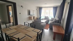 Un salon comprenant un ensemble de canapés, un téléviseur et un coin repas avec une table et des chaises.