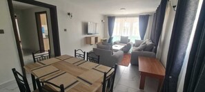 A living room with a sofa set, a TV, and a dining area with a table and chairs. - Mbugani View Suites (Ongata Rongai)