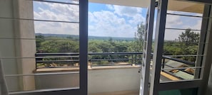 A balcony with a metal railing, a clear view of a green landscape, and a partly cloudy sky. - Mbugani View Suites (Nairobi)