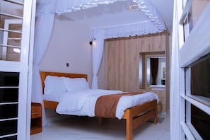 A bedroom with a wooden bed, white bedding, a nightstand, a wooden wardrobe, and a window with curtains. - Mbugani View Suites (Ongata Rongai)