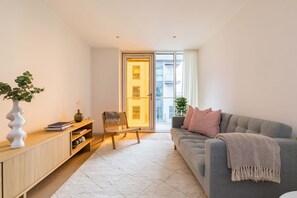 Ein modernes Wohnzimmer mit einem grauen Sofa, einer Holzkommode, einer weißen Vase und einem Sessel.