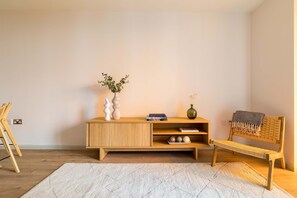Ein Zimmer mit einer hölzernen Bank, einem weißen Teppich, einer Holzkommode mit Büchern und Dekoration sowie einem kleinen Holztisch.
