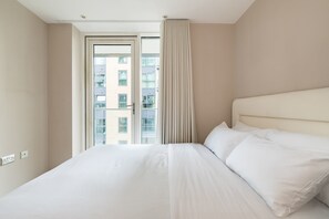 Ein Hotelzimmer mit einem großen Bett, einem Fenster mit Vorhängen und Blick auf Gebäude.