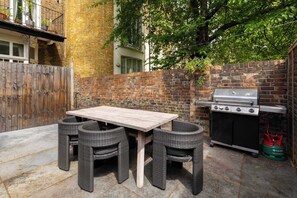 A patio with a table and chairs, a grill, and a gas canister. - Brass & Shaker Clapham (London)