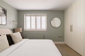 Ein Schlafzimmer mit einem Bett, einem runden Spiegel, einem Fenster mit Jalousien, einem Heizkörper und einem Kleiderschrank.