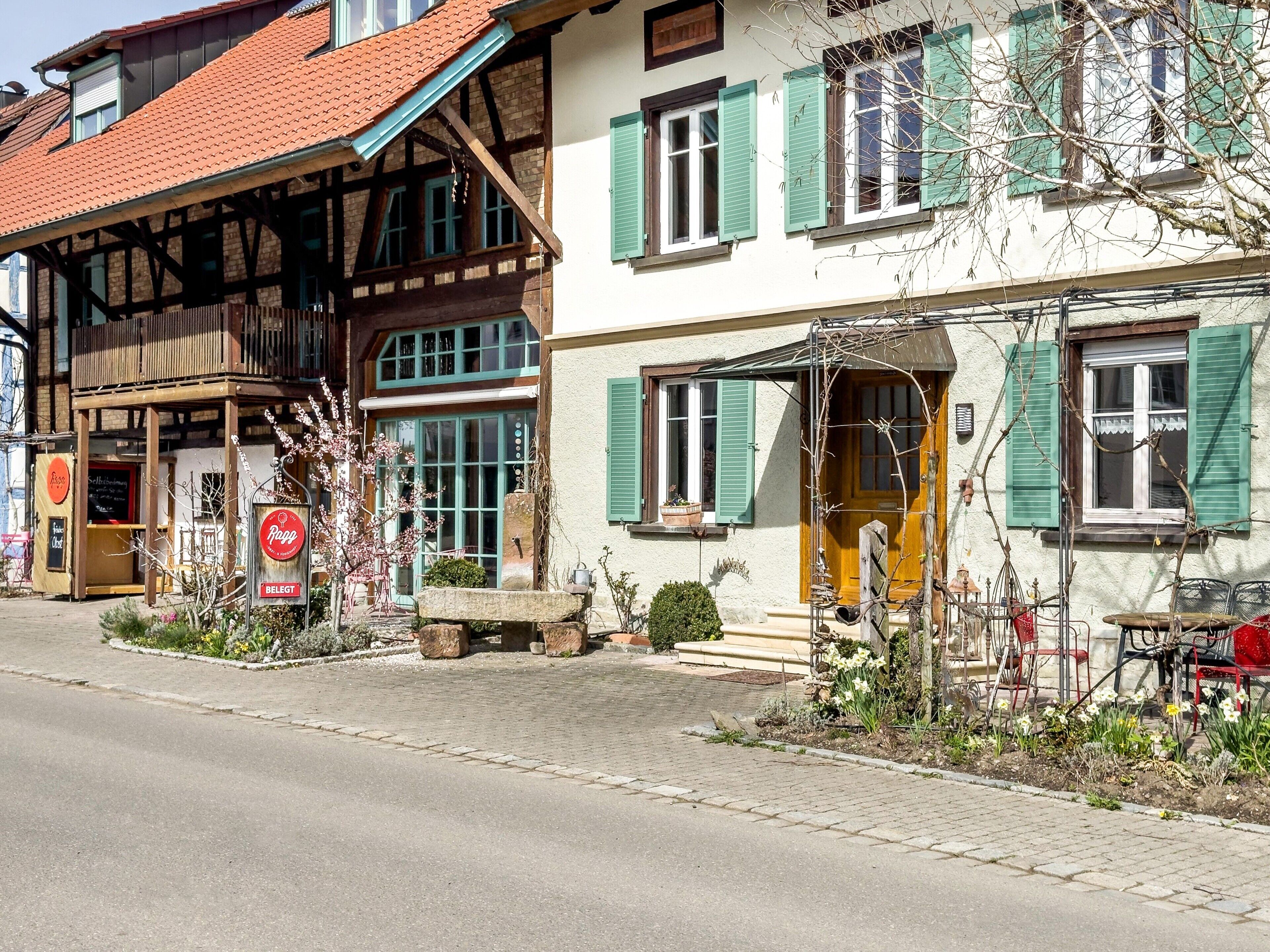 Un edificio tradicional europeo con fachada de madera, ventanas grandes con contraventanas y un banco de piedra en el exterior.