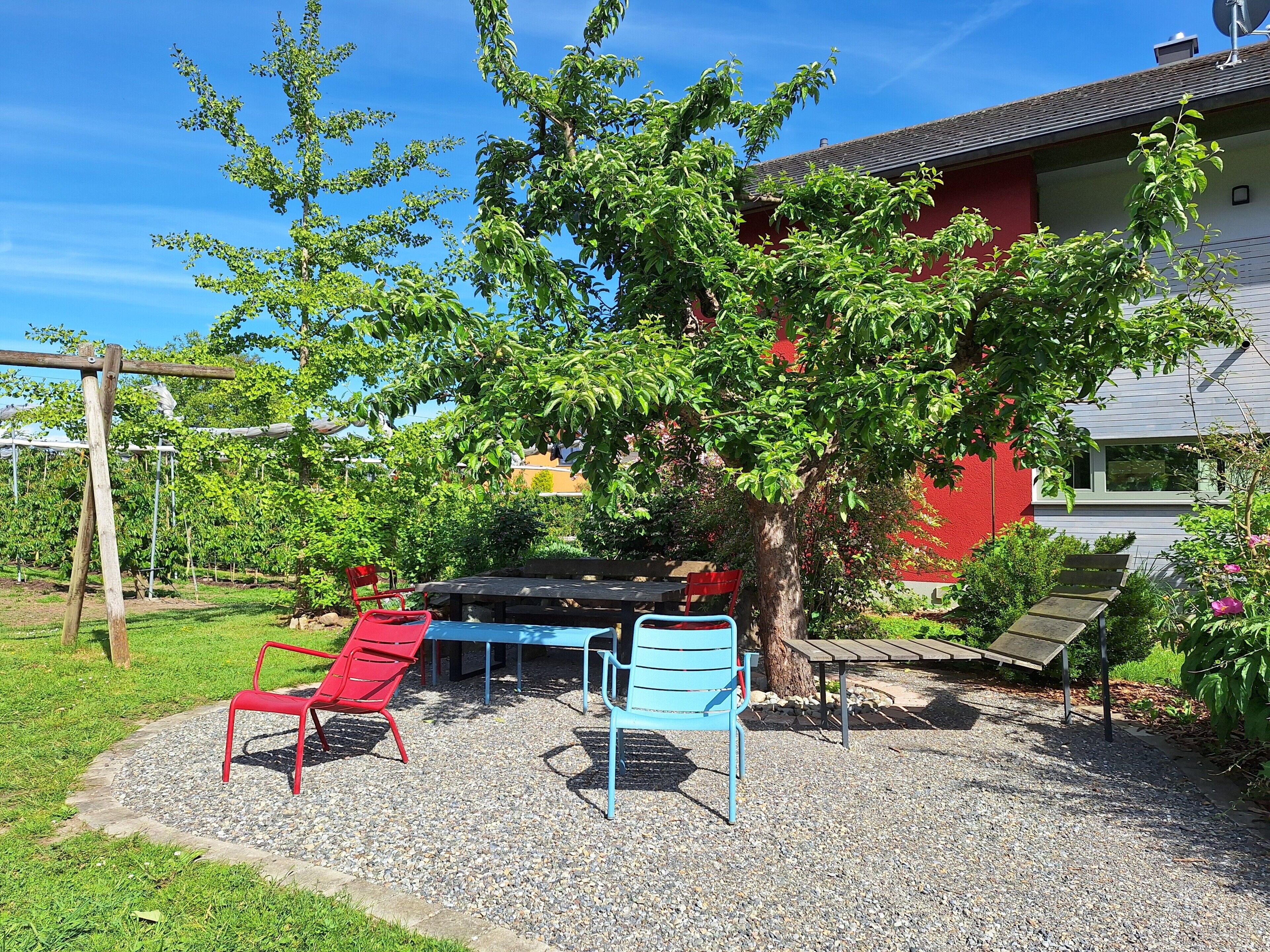 A garden with a table and chairs, a tree, and a building in the background.