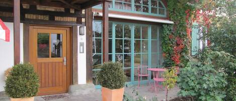 Un edificio con un balcón de madera, una puerta decorada con un corazón y una ventana con contraventanas verdes.