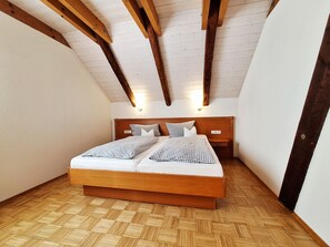 Ein Schlafzimmer mit einem hölzernen Bett, einer schrägen Decke und einem Fischgrätparkett.