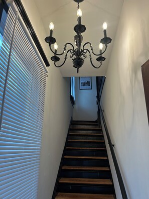 Una escalera con escalones de madera y barandilla negra, que conduce a un rellano con un candelabro.
