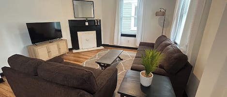 A living room with a sofa set, a TV, a fireplace, and a window with curtains.