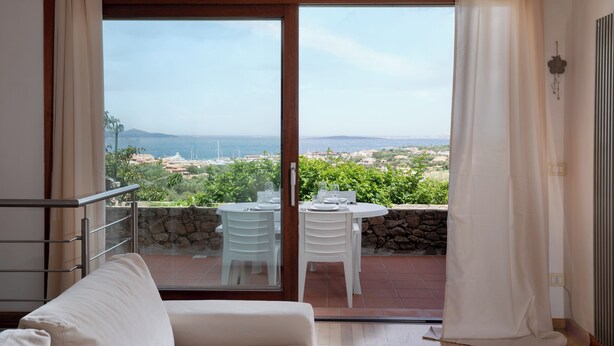 Ein Balkon mit Tisch und Stühlen, ein weißes Sofa und Meer- und Landschaftsblick.