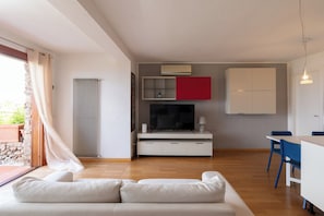 A modern living space with a sofa, a TV, a dining area, and a kitchen. - Casa Aldìa Manna by Wonderful Italy (Porto Rotondo)