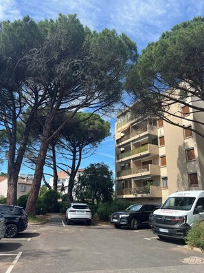 A parking lot with several cars, a multi-story building with balconies, and large trees. - Newly renovated apartment in the center of Saint Raphaël. (Saint-Raphaël)