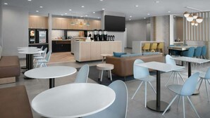 Un interior moderno con mesas y sillas redondas, una zona de cocina y un área de estar con sofá y sillas.