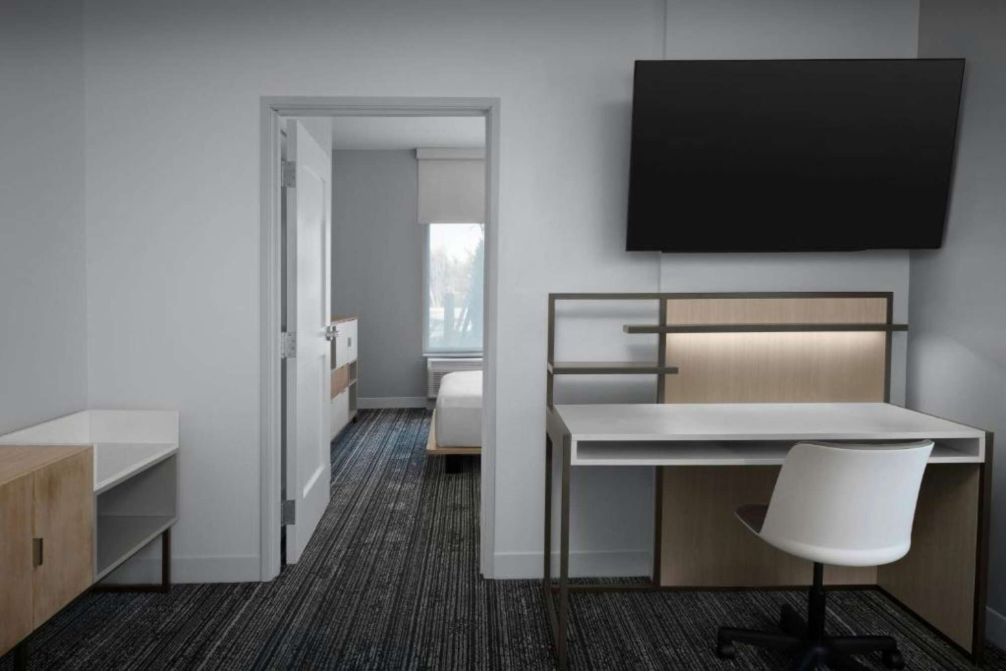 A hotel room with a desk, chair, and a TV mounted on the wall.
