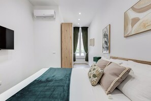 A modern hotel room with a bed, a TV, an air conditioner, a window with curtains, and artwork on the walls. - Heart St Peter - Rome Dream Home (Roma)