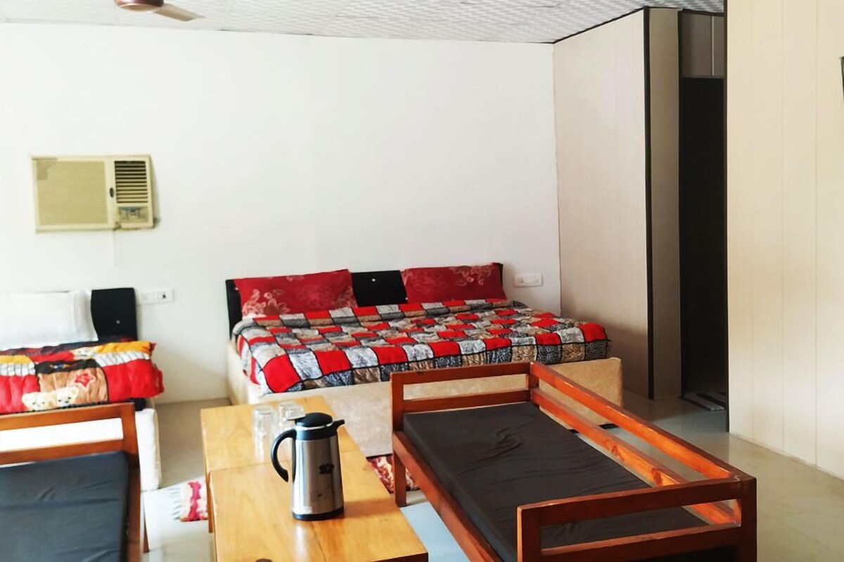 A small, compact room with a single bed, a wooden table, a chair, and a coffee maker.