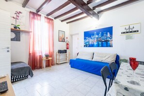 Ein Zimmer mit einem blauen Sofa, einem Tisch mit zwei roten Gläsern, einem Stadtbild und einem kleinen Topfpflanzen.