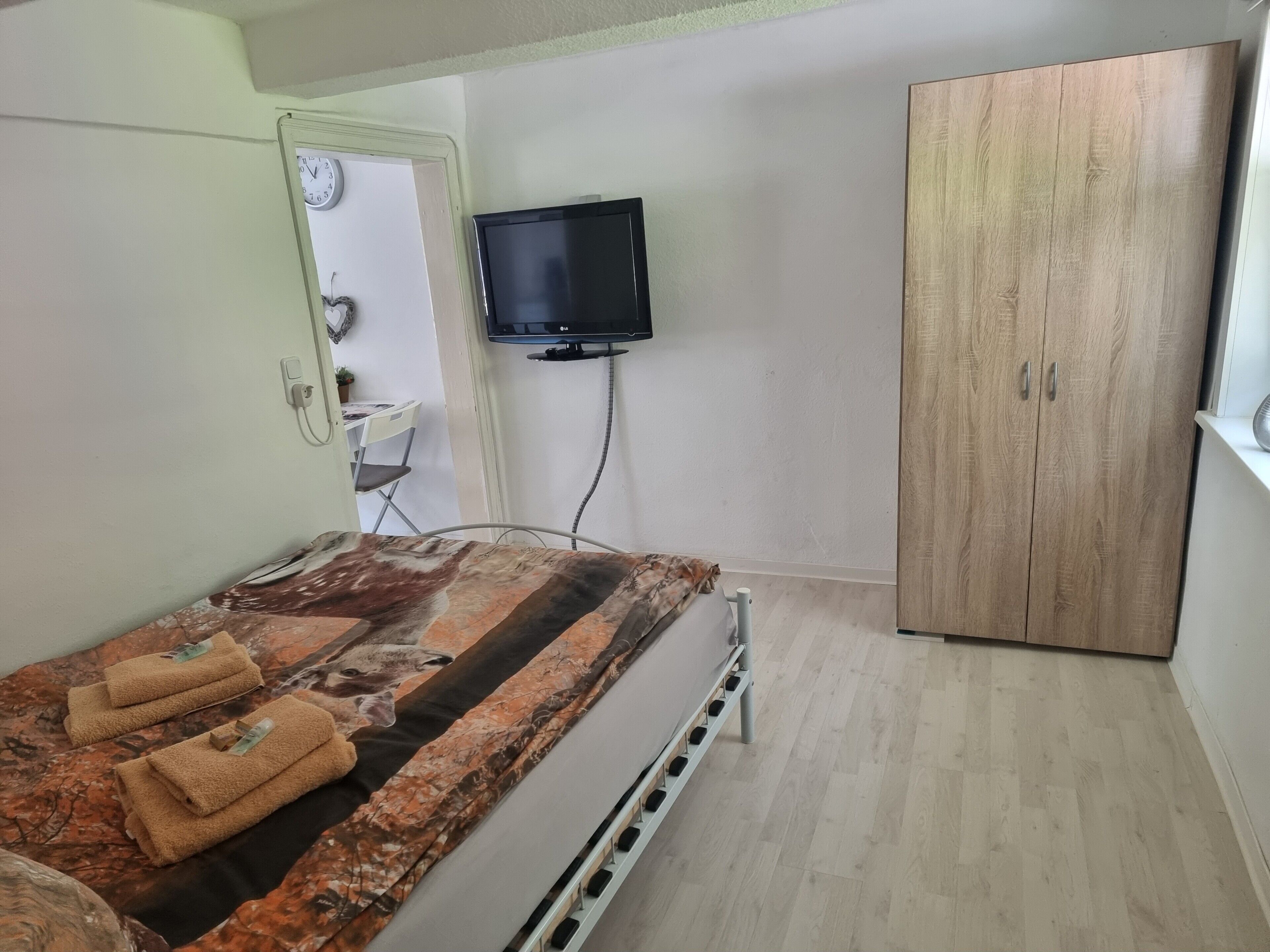 Un dormitorio con cama, televisión, armario y una pequeña mesa con silla.
