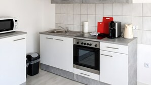 A compact kitchen with a built-in microwave, a sink, a stove, and a trash bin. - Apartment 'Rehkitz' with Mountain View (Bad Lauterberg im Harz)